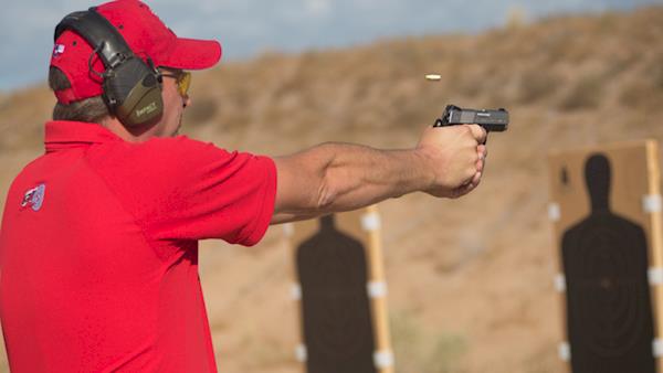 Competitor in a Red Polo Shirt and Cap Firing at Silhouette Targets on an Outdoor Range
